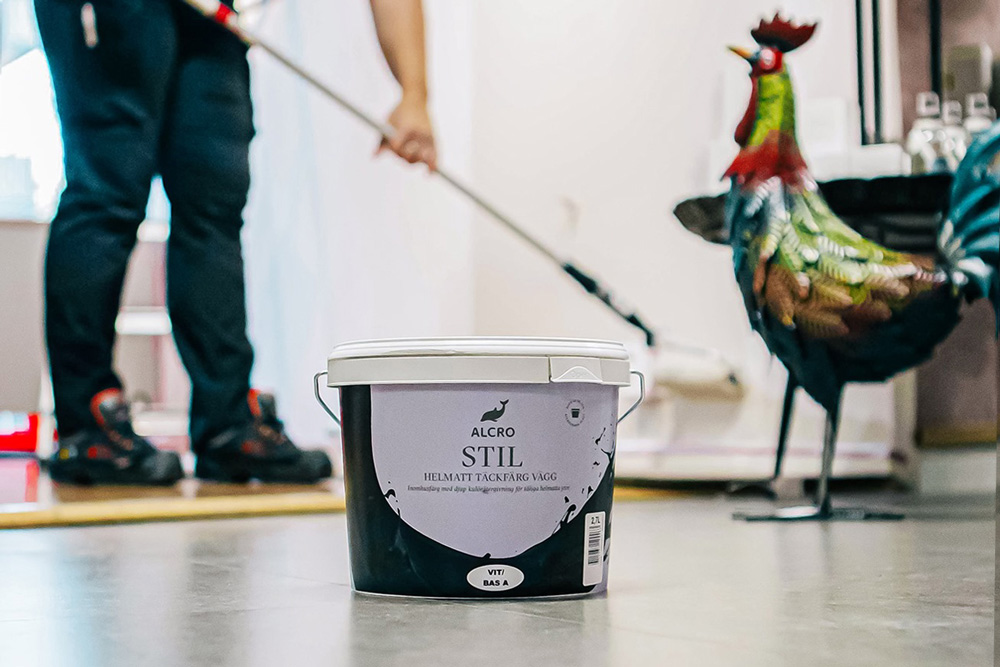 Målarburk i förgrunden med en man som målar en vägg i bakgrunden