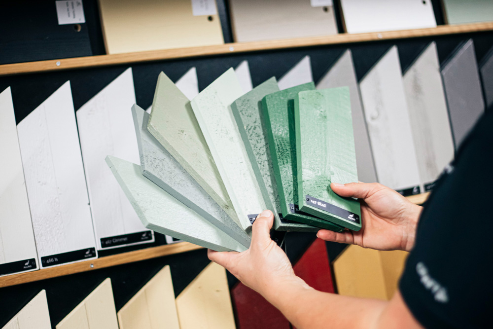 En person håller upp träplankor med olika gröna målarprover